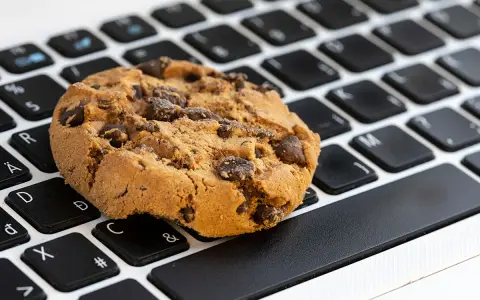 Ciasteczko z kawałkami czekolady leży na klawiaturze laptopa. Czy to są ciasteczka, które śledzą Twoje kliknięcia?