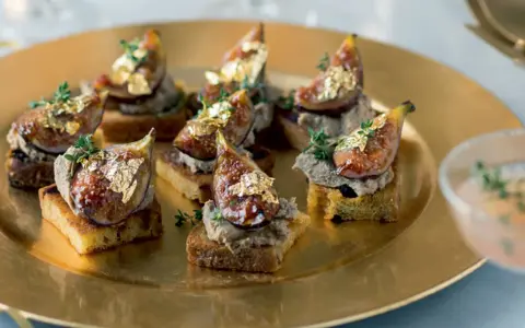 Deliciosos higos con foie sobre tostadas, adornados con pan de oro y tomillo, servidos en una bandeja dorada.
