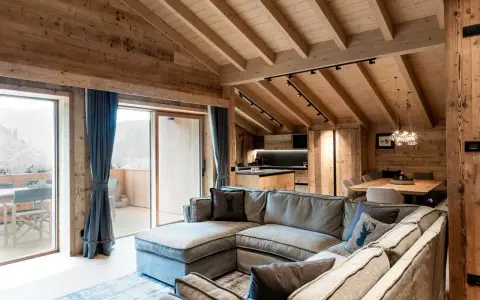 Cozy mountain chalet living room with sectional sofa, wooden beams, and large windows.