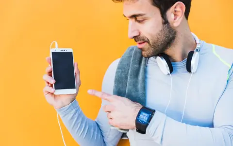 Mężczyzna w sportowym ubraniu pokazuje telefon, jak sparować zegarek z telefonem. Na nadgarstku ma smartwatch.