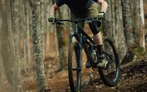 Rowerzysta w kasku i ochraniaczach pokonuje leśny szlak na rowerze górskim, jednym z wielu rodzajów rowerów do jazdy terenowej.
