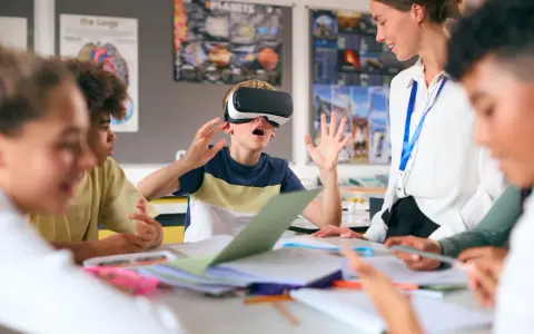 Chłopiec w goglach VR przeżywa lekcję, a nauczycielka z uśmiechem obserwuje tę innowację pedagogiczną.
