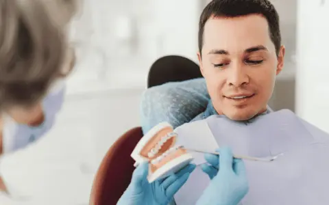 Dentysta pokazuje pacjentowi model szczęki z aparatem ortodontycznym, omawiając, czy trzeba usuwać ósemki do aparatu ortodontycznego.