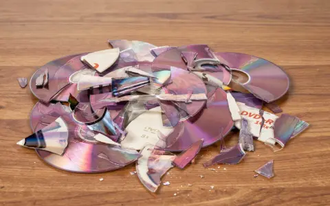 Stos zniszczonych płyt DVD i CD na drewnianym blacie. Czy płyty CD to elektrośmieci? Pytanie o ich utylizację nabiera sensu.