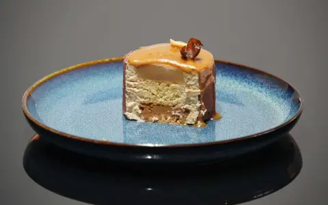 Tranche d'entremet aux couches aériennes, surmontée d'un glaçage caramel et d'une noisette croquante. Le biscuit noisette pour entremet offre une texture légère et savoureuse.