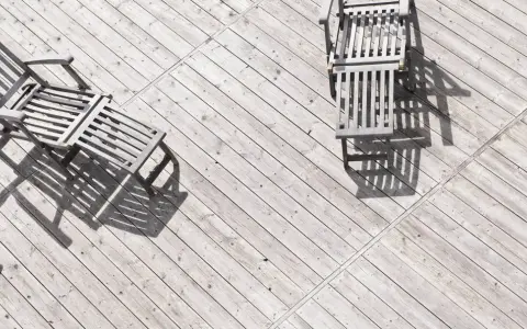 Tre solstolar i trä står på en sliten altan. Solen kastar långa skuggor över siox trall.