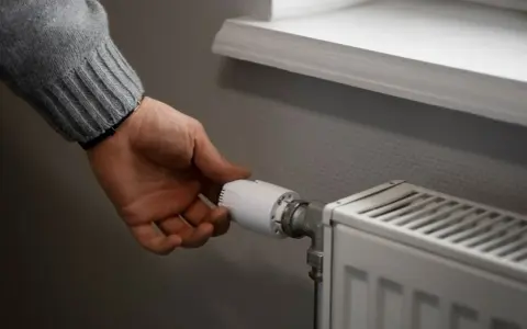 Dłoń reguluje termostat grzejnika. To przykład histerezy, czyli opóźnienia reakcji systemu na zmianę.