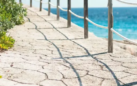 Camino de piedra con barandilla y mar azul. Un ejemplo de cómo hacer hormigón impreso para exteriores.