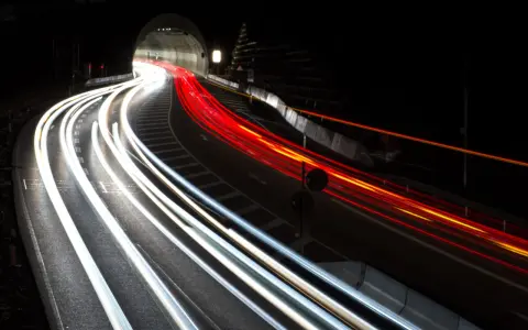 Voiture traversant un tunnel la nuit, capturant les traînées lumineuses des phares et des feux arrière grâce à des photos pose longue.