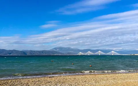 Spokojne morze i plaża w Grecji w styczniu. W oddali widać most Rio-Antirio i góry.