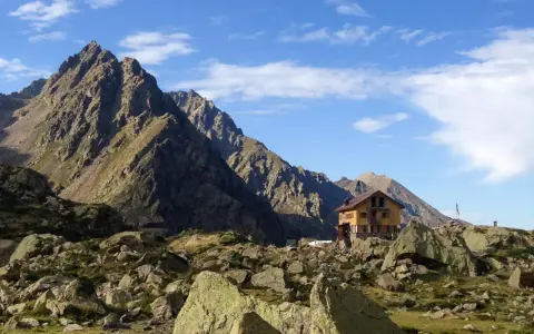 Il rifugio Genova, incastonato tra imponenti montagne rocciose e un cielo azzurro punteggiato di nuvole, offre un riparo solitario e suggestivo.