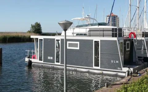 Modernes Hausboot "ULM" im lelystad hafen, umgeben von Schilf und Segelbooten.