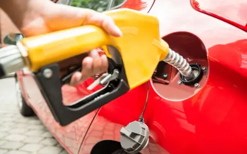 En hand håller en gul pump för att tanka en röd bil. Undrar du vad kostar diesel i Norge?