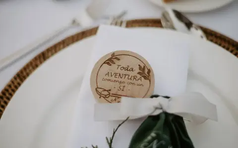 Detalle de mesa de boda con un distintivo de madera que dice "Toda aventura comienza con un SÍ". Ideas para nombres de mesas de boda.