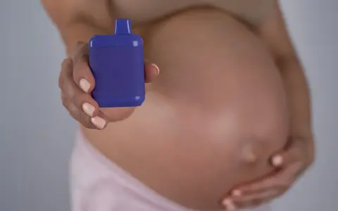 Mujer embarazada sostiene un vapeador morado, sugiriendo la opción de vapear embarazo sin nicotina.