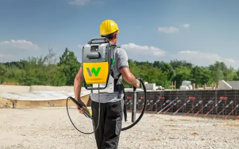 Bauarbeiter mit Rucksackeinheit und Rüttler zur Beton verdichten auf einer Baustelle.
