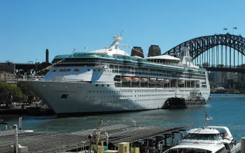 La Rhapsody of the Seas, un'imponente nave da crociera, attracca nel porto di Sydney, con l'iconico ponte sullo sfondo.