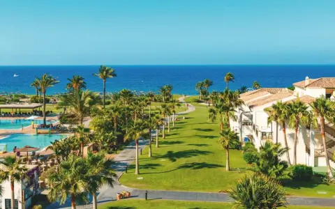 Traumhafter Blick auf das Granada Meer, Palmen säumen den Weg zum Pool und den weißen Hotelgebäuden.
