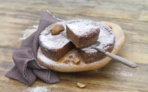 Gâteau au chocolat saupoudré de sucre glace, avec des châtaignes. Une part est coupée, prête à être dégustée. Une recette de châtaigne à essayer !