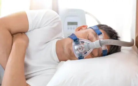 Mężczyzna śpi z maską CPAP, która pomaga mu oddychać podczas bezdechu sennego.