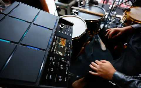 Nowoczesny sampler perkusyjny Roland SPD-SX PRO gotowy do tworzenia rytmów. W tle widoczne elementy zestawu perkusyjnego.