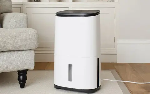 Un deshumidificador blanco moderno junto a un sillón gris, ideal para saber como elegir un deshumidificador y mejorar el ambiente de tu hogar.