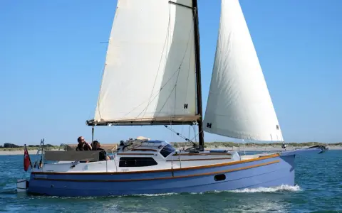 Eine blaue Baycruiser 26 segelt auf ruhigem Wasser unter klarem Himmel. Zwei Personen genießen die Fahrt.