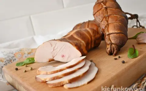 Wędzona pierś z kurczaka, pokrojona w plastry, leży na desce obok całych kawałków.