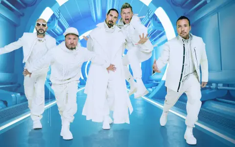 Backstreet Boys w białych strojach, gotowi na koncert. Ich energia jest zaraźliwa, a futurystyczna scenografia podkreśla ich styl.