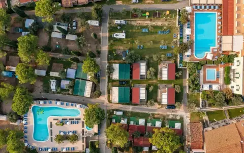Widok z lotu ptaka na camping Toscolano: domki, baseny, przyczepy kempingowe i zielone tereny.