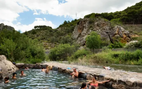 Gente disfrutando de las piscinas naturales en La Rioja, rodeadas de vegetación y rocas.