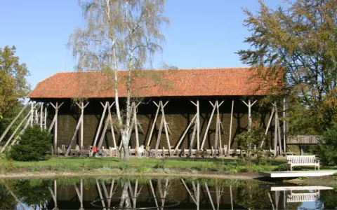 Große Gradierwerke mit roten Ziegeldächern, umgeben von Bäumen und einem Teich. Hier wird die Luft mit gesundem **saline rheine** angereichert.