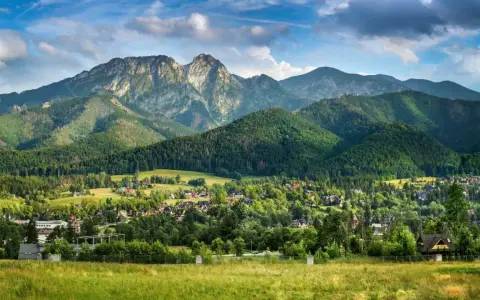 Widok na Giewont, majestatyczny szczyt o imponującej wysokości, otoczony zielonymi lasami i malowniczą wsią u podnóża.