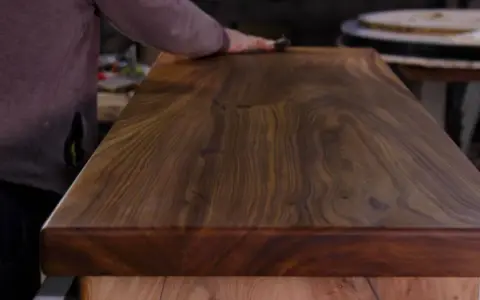 Main d'artisan polissant un plateau en bois de noyer, révélant la beauté du grain pour un traitement naturel bois parfait.