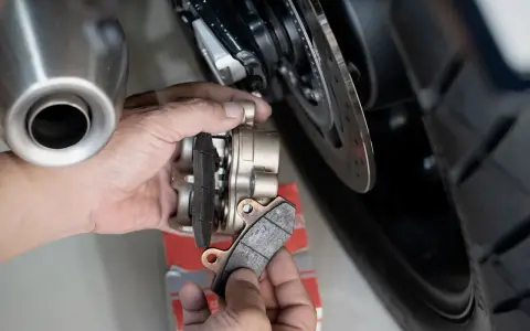Mani che sostituiscono le pastiglie dei freni anteriori di una moto. Si valuta la durata pastiglie freni anteriori osservando l'usura.