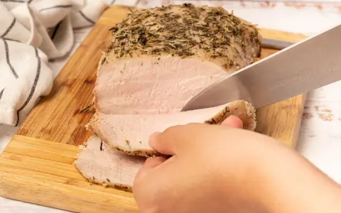 Un jugoso lomo a la sal, cubierto de hierbas, se corta en rodajas tiernas sobre una tabla de madera.