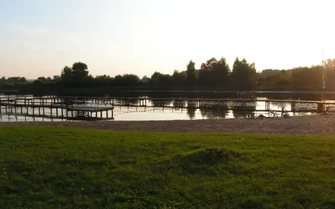 Drewniane pomosty na spokojnym jeziorze starogrodzkim, z piaszczystą plażą i zieloną trawą w tle.