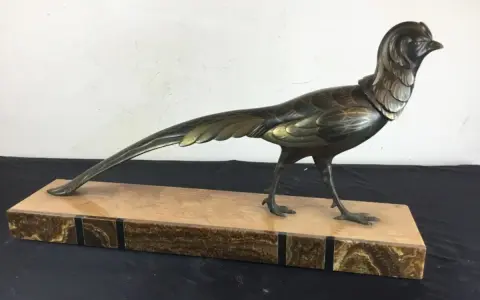 Sculpture d'oiseau en bronze, style Irénée Rochard, sur un socle en marbre veiné. L'oiseau, aux détails fins, arbore une longue queue élégante.