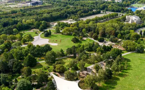 Luftaufnahme eines weitläufigen **Parks in Dortmund** mit grünen Rasenflächen, verschlungenen Wegen, blühenden Beeten und dichtem Baumbestand.
