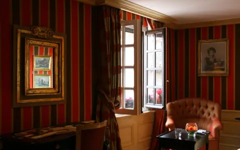 Fenêtre ouverte et miroir pour comment éclaircir une pièce sombre. Un fauteuil confortable et un bureau complètent ce décor.