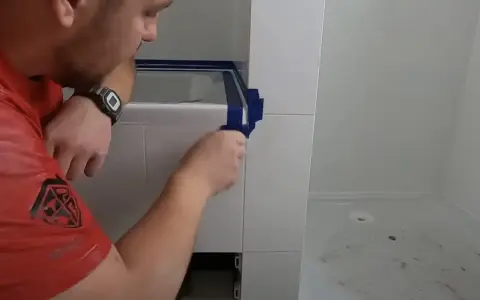 Mężczyzna okleja taśmą krawędzie płytek, przygotowując się do aplikacji fugi epoksydowej. Unikanie błędów to klucz do sukcesu.