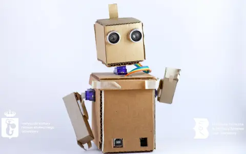 Uroczy robot z kartonu, z oczami-sensorami i kolorowymi kablami, gotowy do nauki i zabawy.