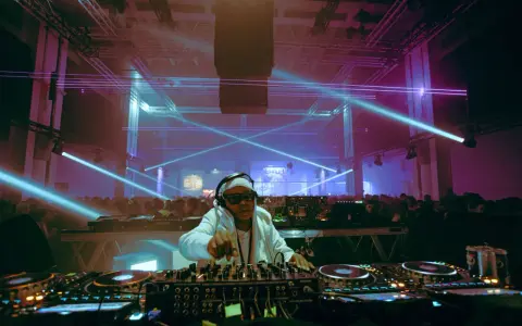 Un DJ année 2000, lunettes de soleil et bandeau, mixe sous des lasers bleus et violets devant une foule en délire.