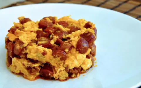 Deliciosa porción de duelos y quebrantos receta, con huevo revuelto y trozos de chorizo, servida en plato blanco.