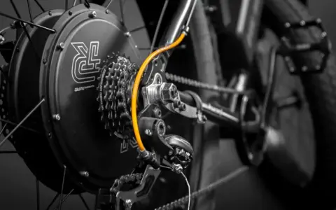 Zestaw do konwersji roweru: czarna piasta z logo, kasetka Shimano, pomarańczowy przewód i przerzutka.