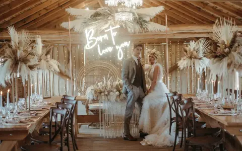 Elegancka sala weselna stodoła z parą młodą, neonem "Born to love you" i boho dekoracjami z traw pampasowych.