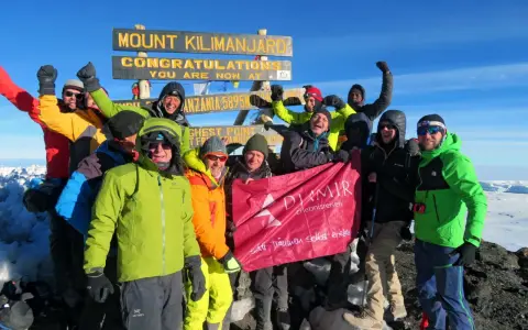 Glückliche Gruppe feiert auf dem Gipfel des Kilimandscharo. Sie haben den Gipfel erreicht und halten ein Banner hoch. Ein unvergessliches Erlebnis, den Kilimandscharo zu besteigen!