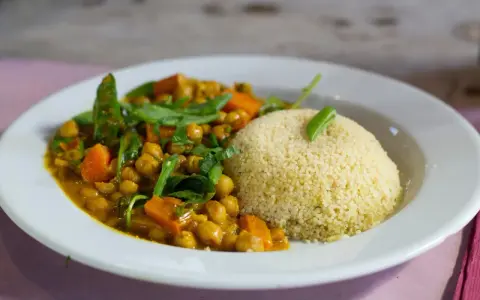 Un plato de cuscus con verduras, garbanzos y zanahoria en una salsa dorada, decorado con hojas verdes.