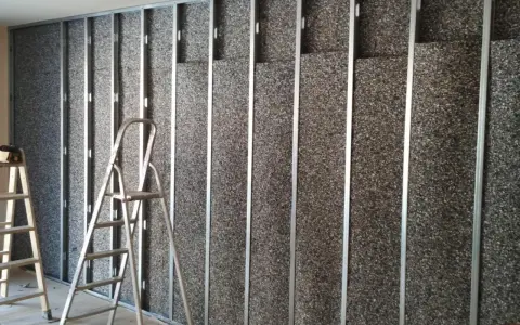 Instalación de material para insonorizar pared. Escaleras apoyadas contra la estructura metálica y el panel aislante.