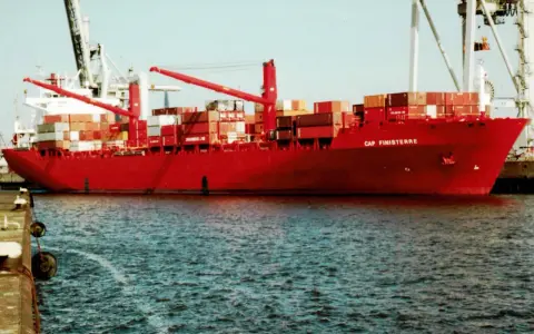 Rotes Containerschiff "Cap Finisterre" im Hafen, beladen mit vielen Containern, Kräne im Hintergrund.
